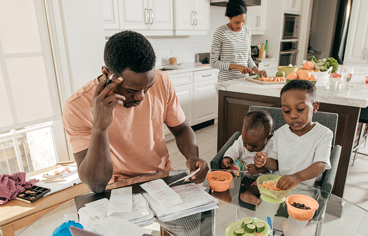 Familia en la cocina, padre usando una calculadora y mirando facturas