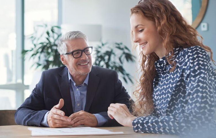 Un homme et une femme se sourient et se parlent tout en regardant des documents sur le bureau devant eux.